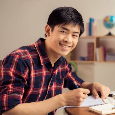 Portrait,Of,Cheerful,Asian,Student,Doing,Homework